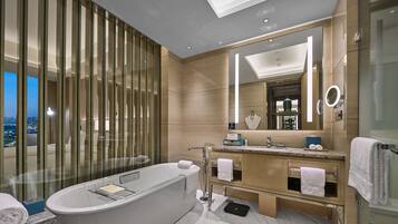 A modern bathroom with a large bathtub, a vanity with a mirror, and a view of the city.