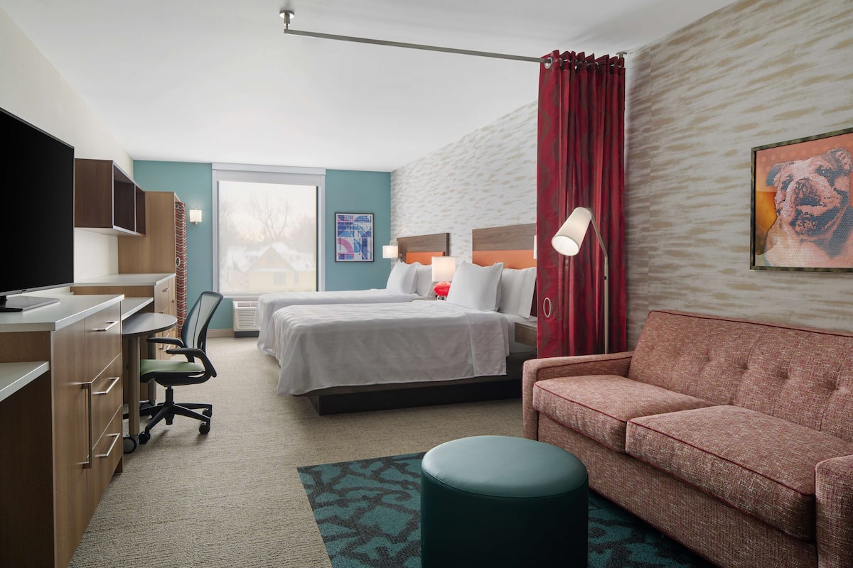 Ein Hotelzimmer mit Bett, Schreibtisch, Stuhl, einer Couch und einem Fernseher.