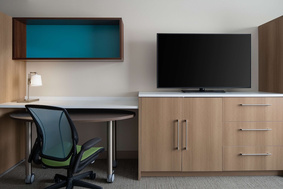 Une chambre d’hôtel moderne équipée d’un bureau, d’une chaise, d’une télévision et d’une armoire intégrée en bois.
