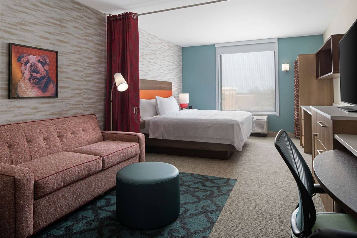 Ein Hotelzimmer mit einer Couch, einem Bett, einem Schreibtisch, einem Stuhl, einer Lampe und einem Fernseher.