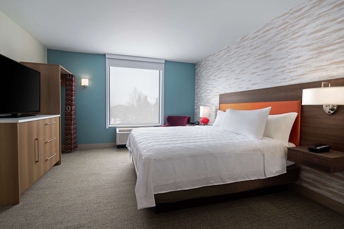 A hotel room with a bed, a television, a desk, and a window.