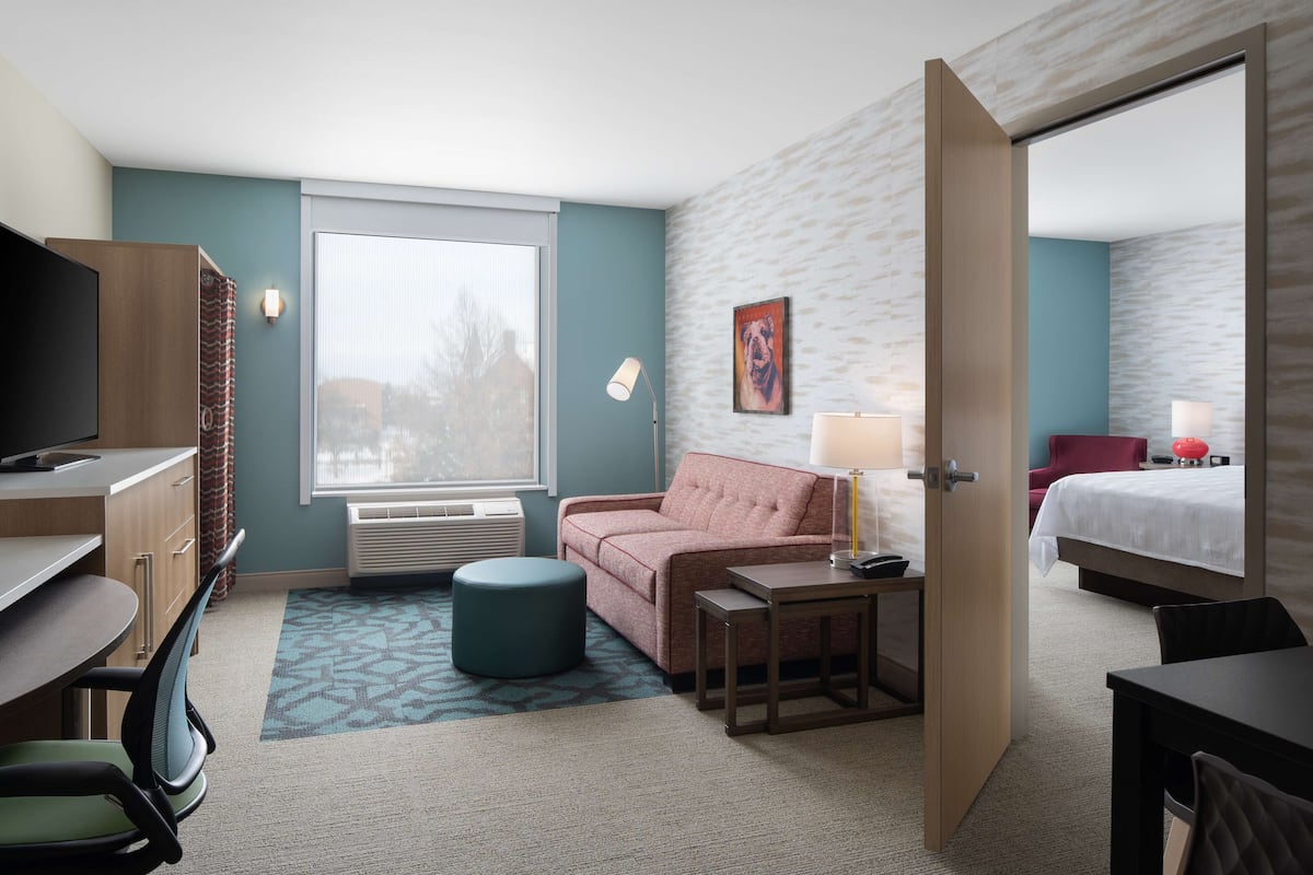 Ein Hotelzimmer mit Schreibtisch, einer Couch, einem Bett, einem Fernseher und einem Fenster.