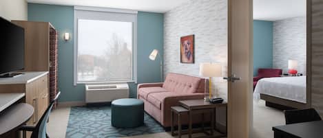 Een hotelkamer met een bureau, een bank, een bed, een televisie en een raam.