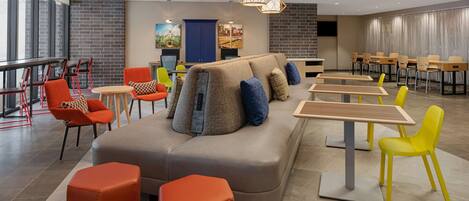 Un espace de détente moderne comprenant un canapé, des poufs et des tables, avec un assortiment de chaises rouges et jaunes.