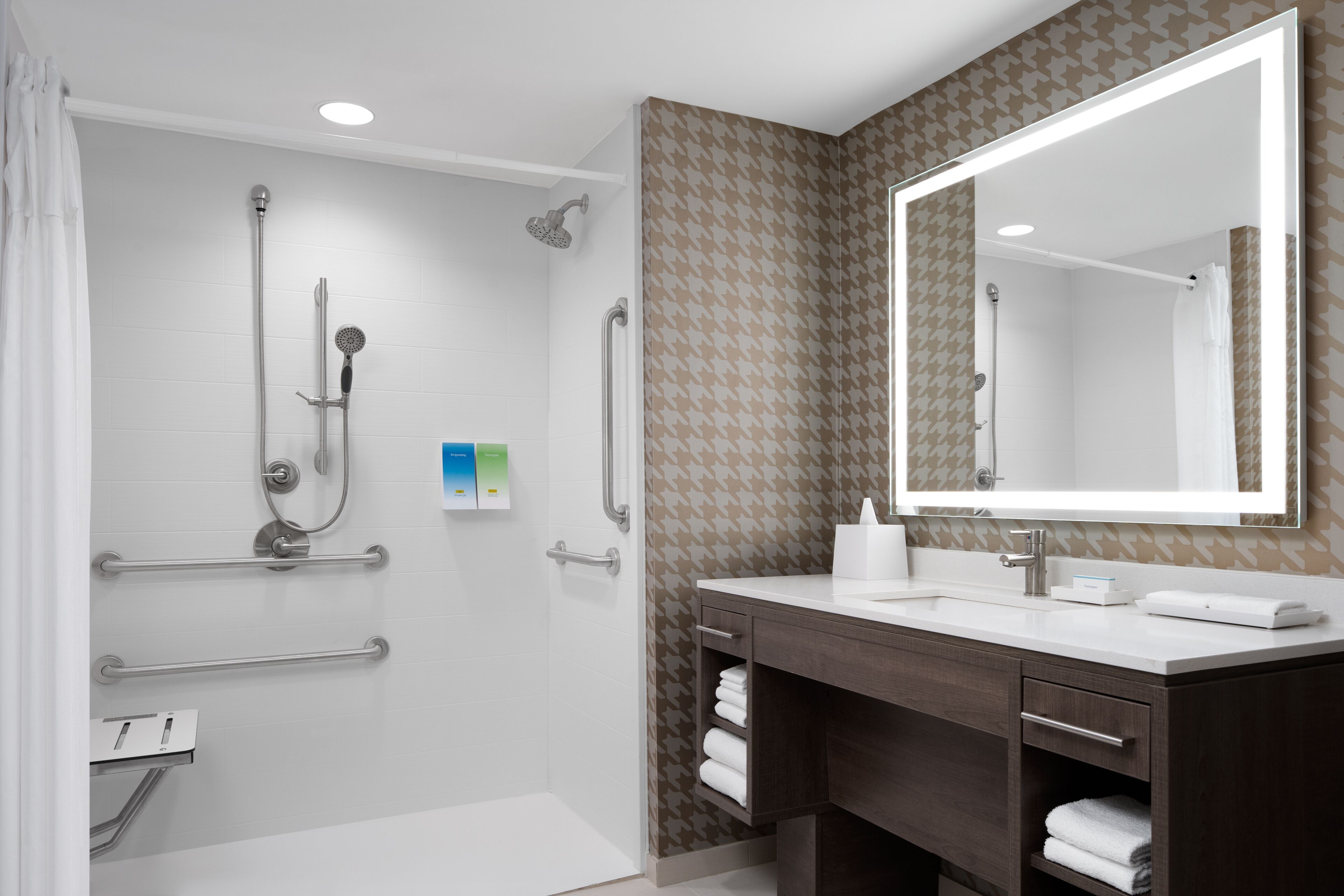 A modern bathroom with a walk-in shower, grab bars, a large mirror, and a vanity with a towel rack.