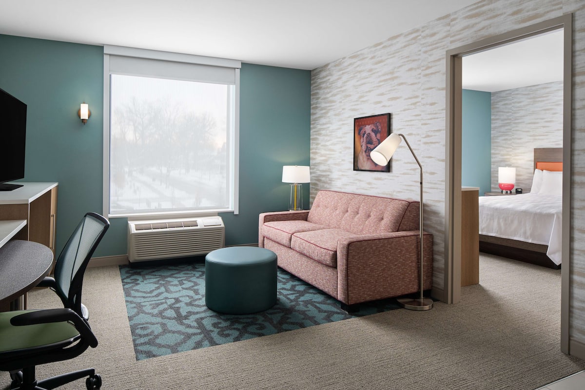 Ein Hotelzimmer mit Schreibtisch, Stuhl, Sofa, Hocker und einem Bett.