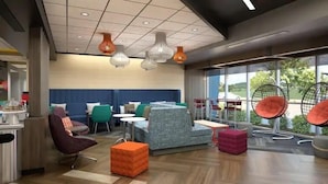 A modern lounge area with seating arrangements, a large window offering a view of the outdoors, and contemporary lighting fixtures. - Tru by Hilton Spartanburg (Spartanburg)