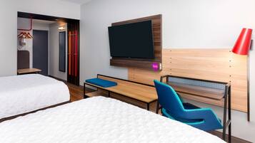 A hotel room with two beds, a desk, a chair, a TV mounted on the wall, and a red lamp.