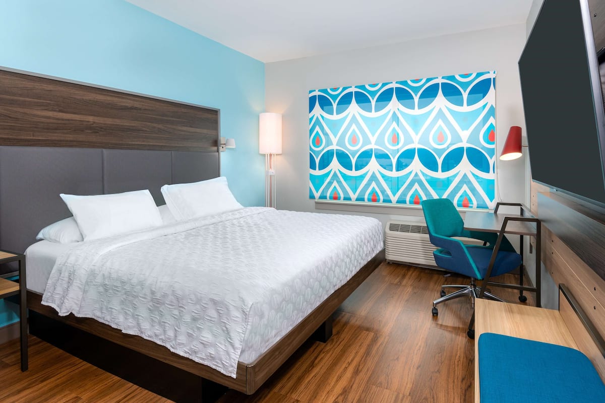 Ein modernes Hotelzimmer mit einem großen Bett, einem Schreibtisch, einem Sessel und einer Wanddekoration.