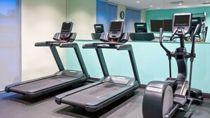 Un gimnasio con cintas de correr, elípticas y un reloj de pared.