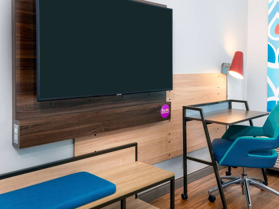 A modern room with a large flat-screen TV mounted on a wooden wall, a desk with a chair, and a bench.