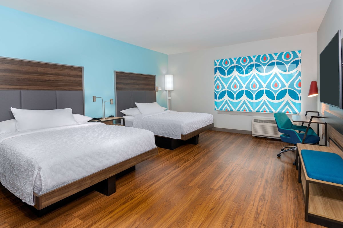 Ein Hotelzimmer mit zwei Betten, einem Schreibtisch, einem Sessel und einem Fernseher, sowie einer Wand mit Muster.