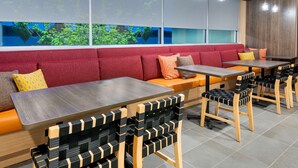 Un restaurante moderno con mesas y sillas de madera, asientos acolchados rojos y grandes ventanales con vistas a zonas verdes.