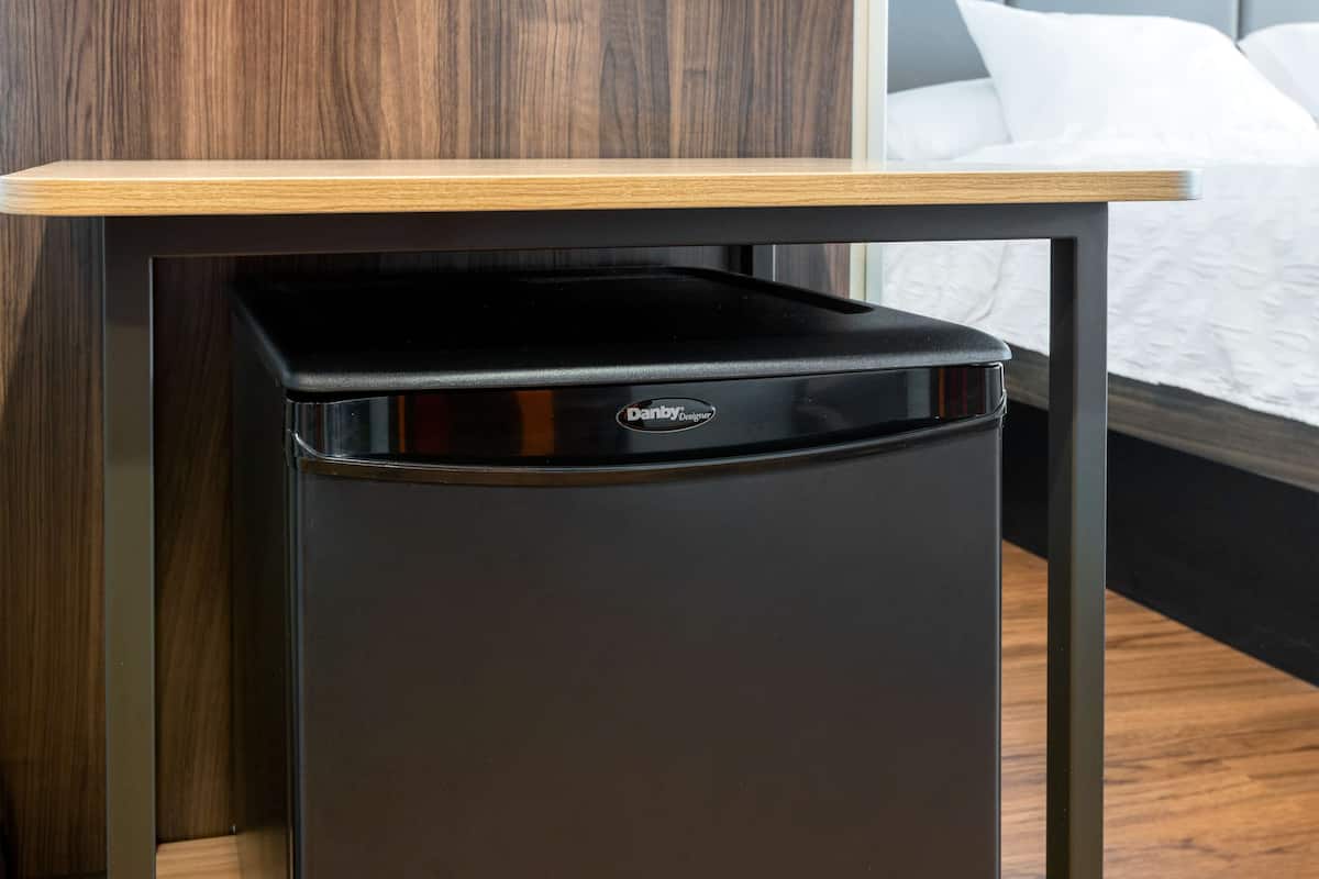 Ein kompakter, schwarzer Danby Designer Kühlschrank mit einer Holztischplatte, platziert unter einem Tisch in einem Hotelzimmer.