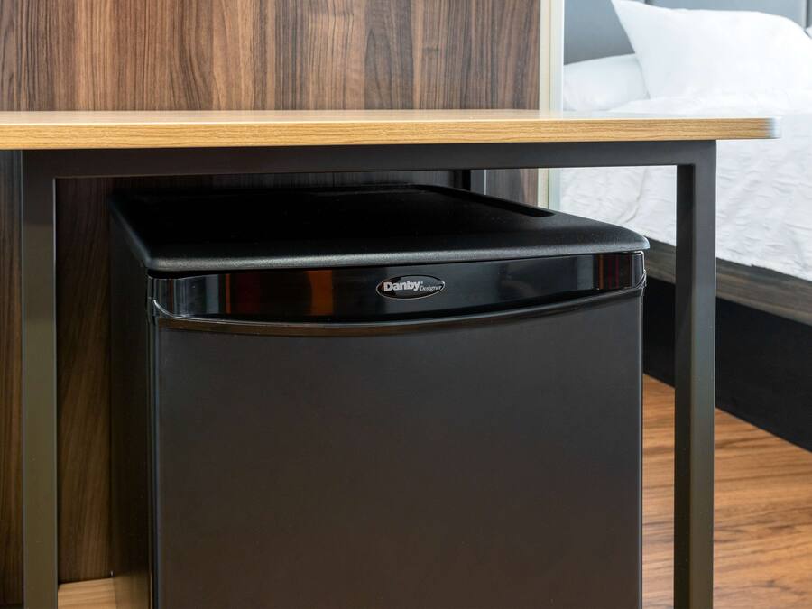 A compact black trash bin with a wooden top, placed on a dark-colored table against a wooden wall.