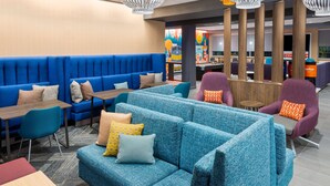 Un área de descanso moderna con asientos azules, mesas de madera y decoración vibrante.