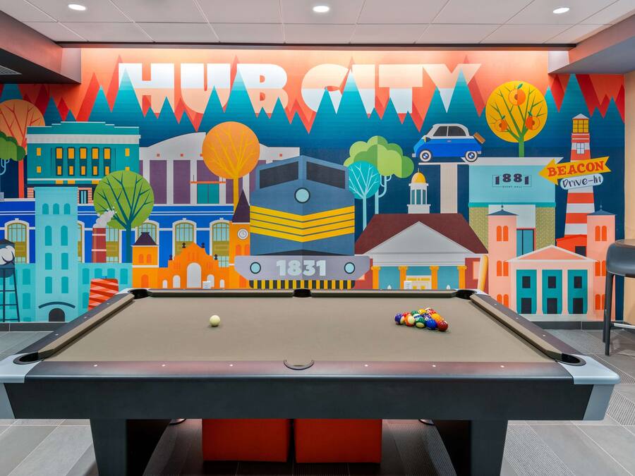 Una mesa de billar con un mural de colores al fondo que muestra un paisaje urbano y la palabra "HURRICUT".