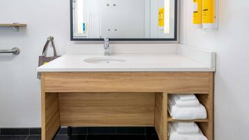 A modern bathroom with a wooden vanity, a large mirror, and a shelf with towels.