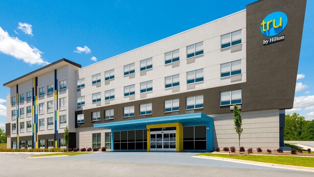 Un hotel moderno con un llamativo letrero de 'tru by Hilton', múltiples ventanas y un exterior bien cuidado.