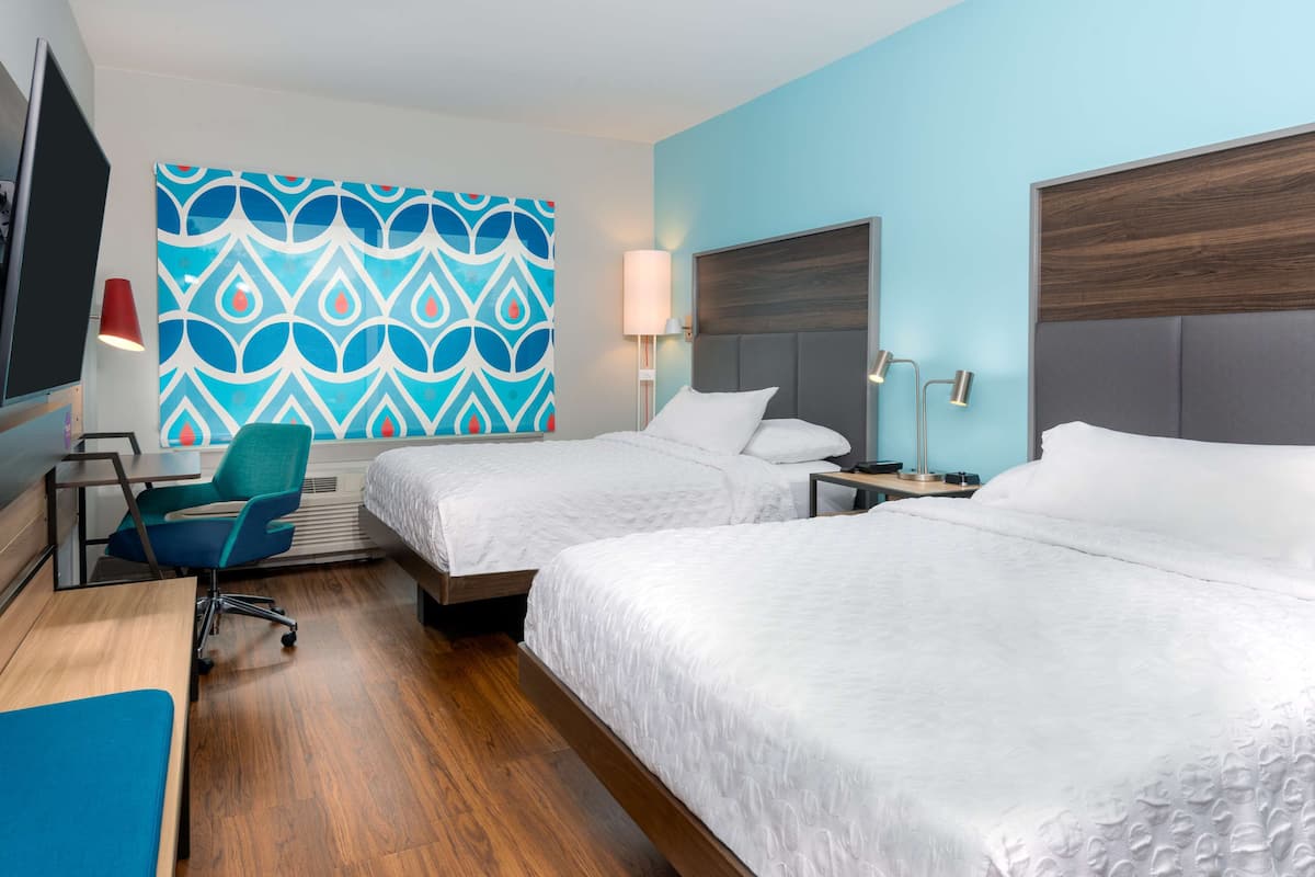 Ein Hotelzimmer mit zwei Betten, einem Schreibtisch mit Stuhl, einem Fernseher und einer Wand mit geometrischem Muster.