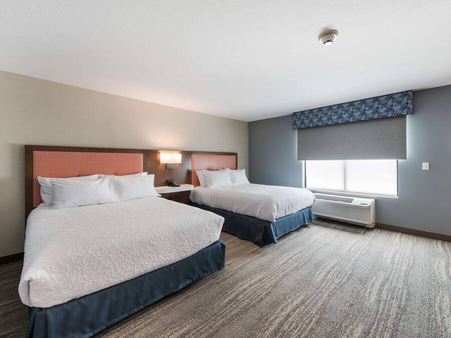 Hotelkamer met twee bedden, een groot raam met uitzicht, een luchtverkoeler aan het plafond en een kunstwerk aan de muur.