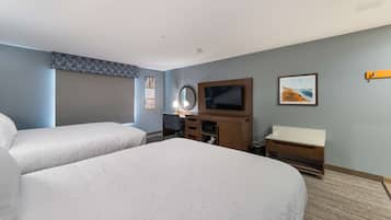A hotel room with two beds, a TV, a desk with a chair, a mirror, and a small cabinet.