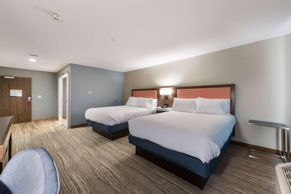 A hotel room with two beds, a desk, and a chair.