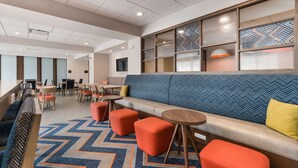 A modern lounge area with a long sofa, orange ottomans, and a patterned carpet.
