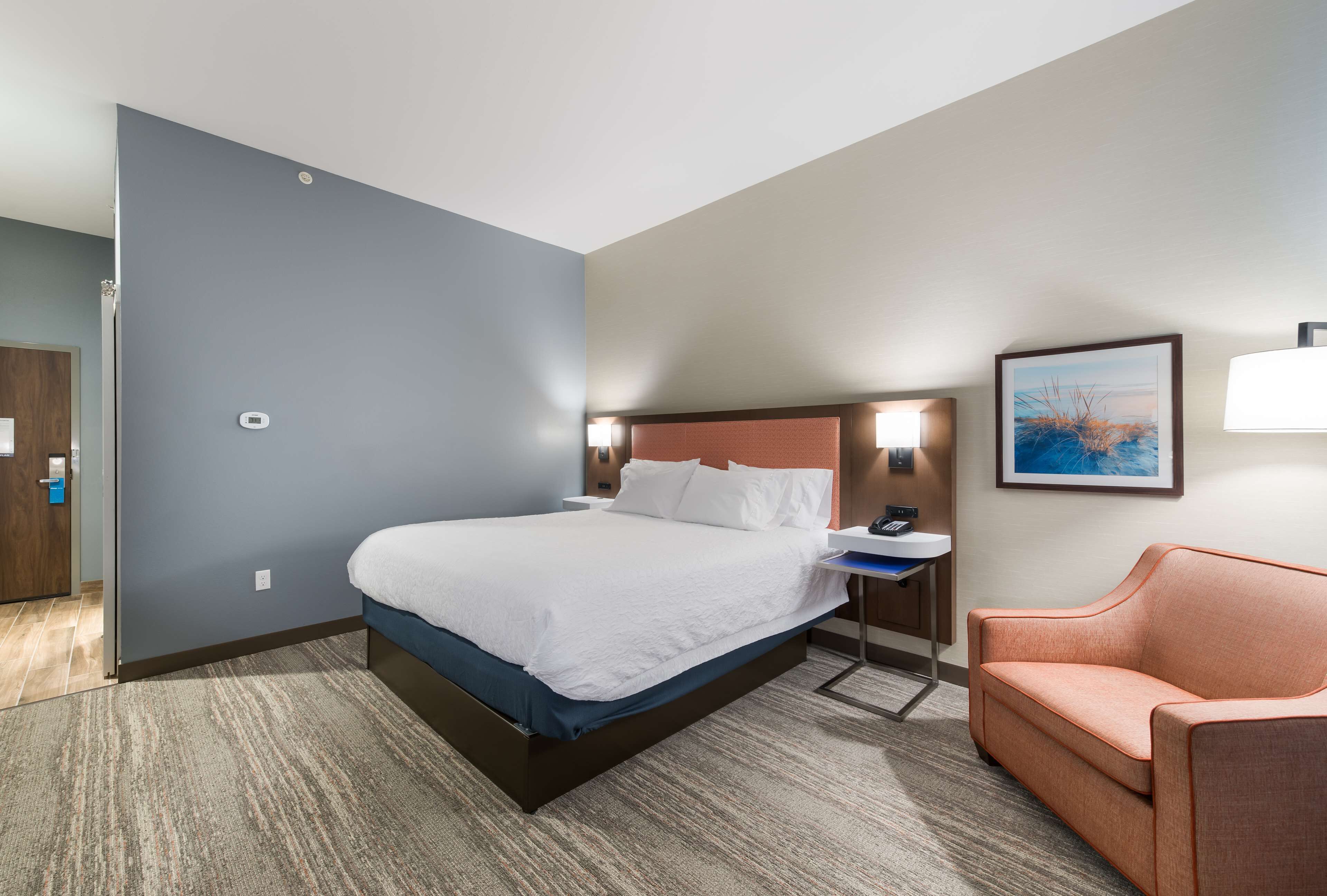 Habitación de hotel con una cama grande, un escritorio, una silla y un cuadro en la pared.