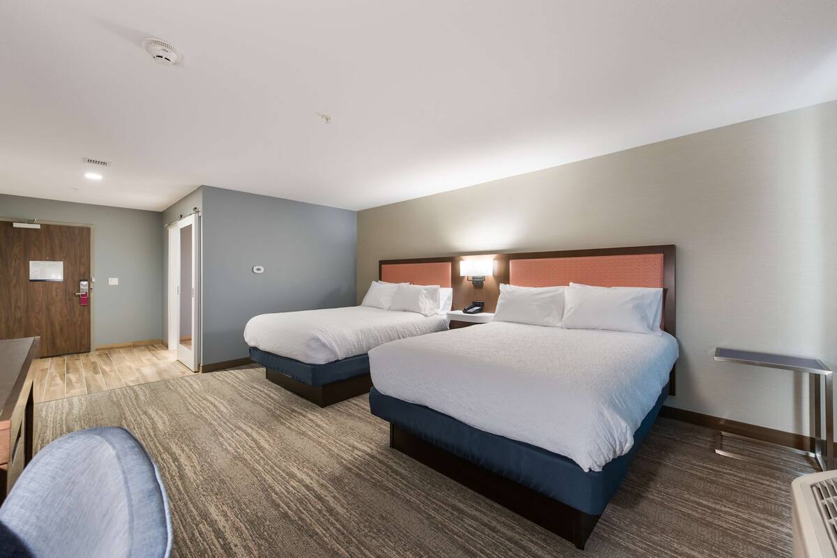 A hotel room with two beds, a desk, and a chair.