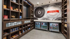 A snack and beverage area with shelves stocked with various snacks and drinks, a clock, and a wall mural with a 'Treats' sign.