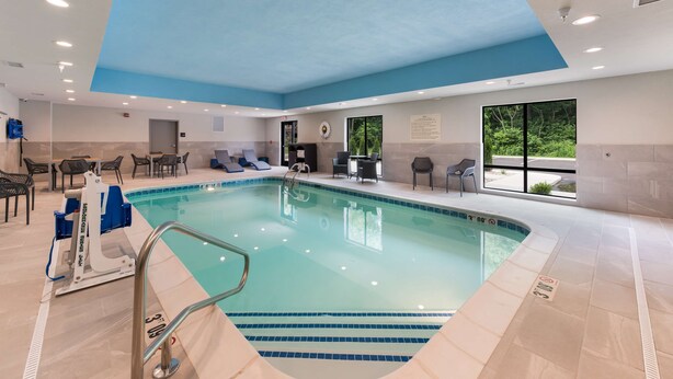 An indoor swimming pool with a blue ceiling, a lifeguard chair, and lounge chairs around the pool.