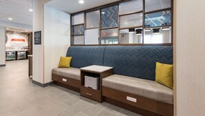 A seating area with a sofa and a small table, a wall with patterned glass panels, and a sign indicating amenities.