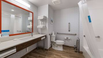 A modern bathroom with a large mirror, white fixtures, a toilet, a shower, and a grab bar.