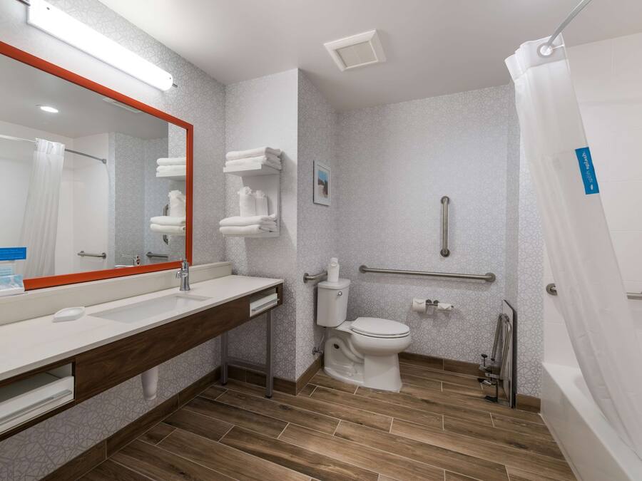 A modern bathroom with a large mirror, white fixtures, a toilet, a shower, and a grab bar.