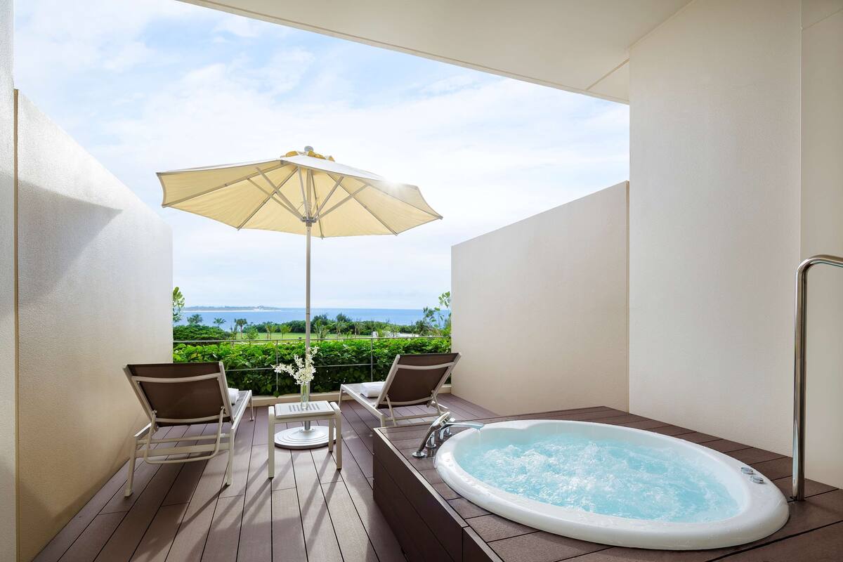 Un balcón con un jacuzzi, dos sillas, una mesa y una sombrilla.