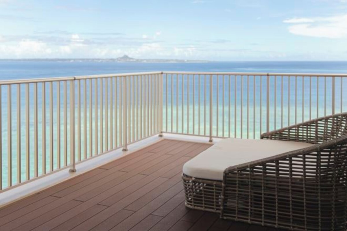 A balcony with a wooden floor and a wicker chair with a cushion.