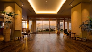 A spacious lobby with wooden flooring, large potted plants, and a view of the sunset through floor-to-ceiling glass doors. - Hilton Okinawa Sesoko Resort (Motobu)