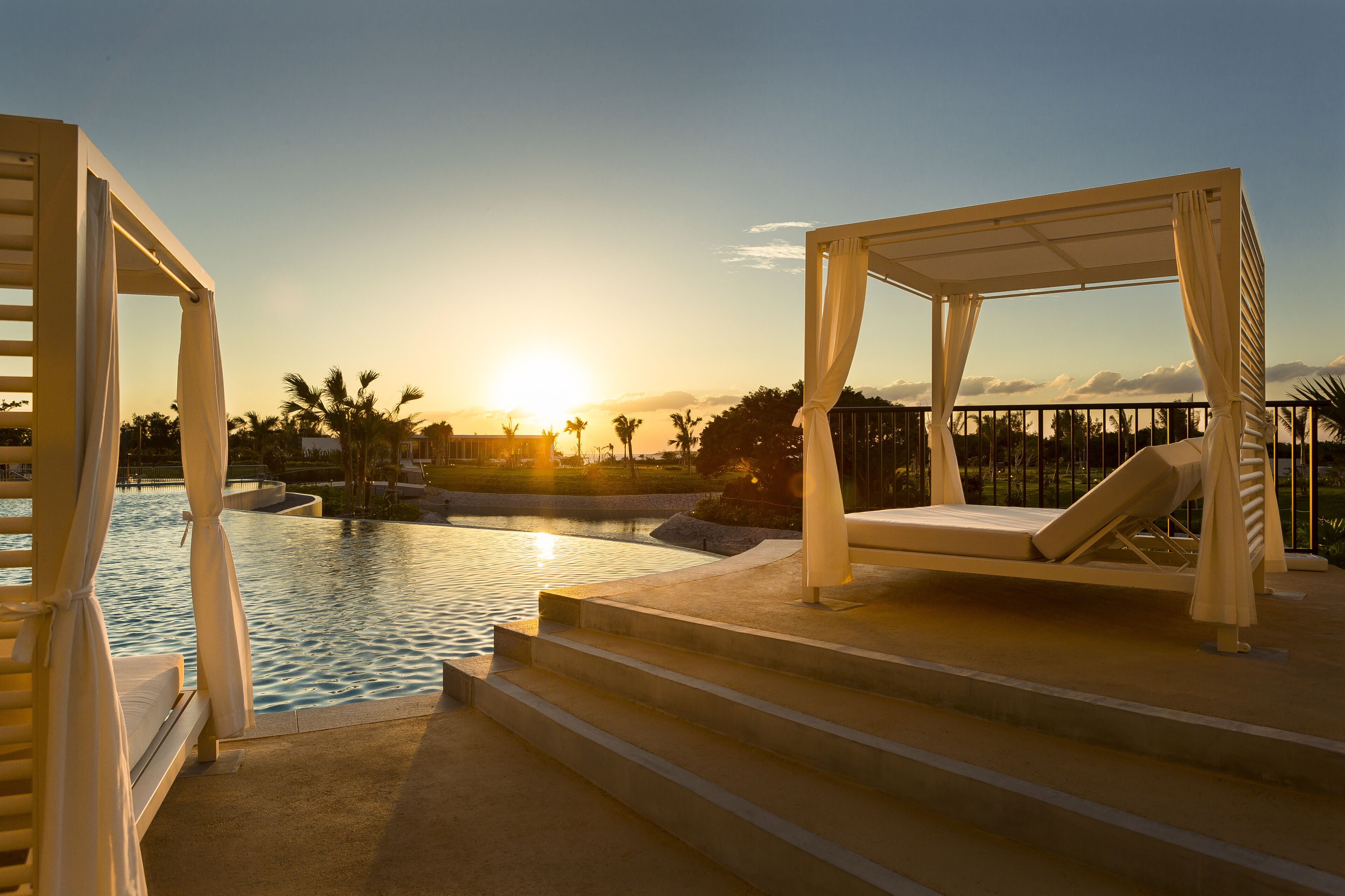 A poolside area with a sunlit sky, a pool, and lounge chairs.