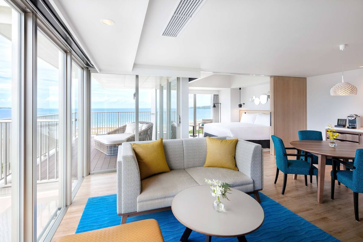 Habitación de hotel moderna con balcón, sofá, mesa de comedor y cama.