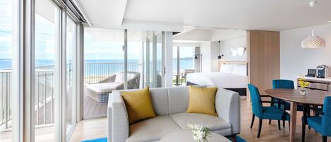 Quarto de hotel moderno com varanda, sofá, mesa de jantar e cama.