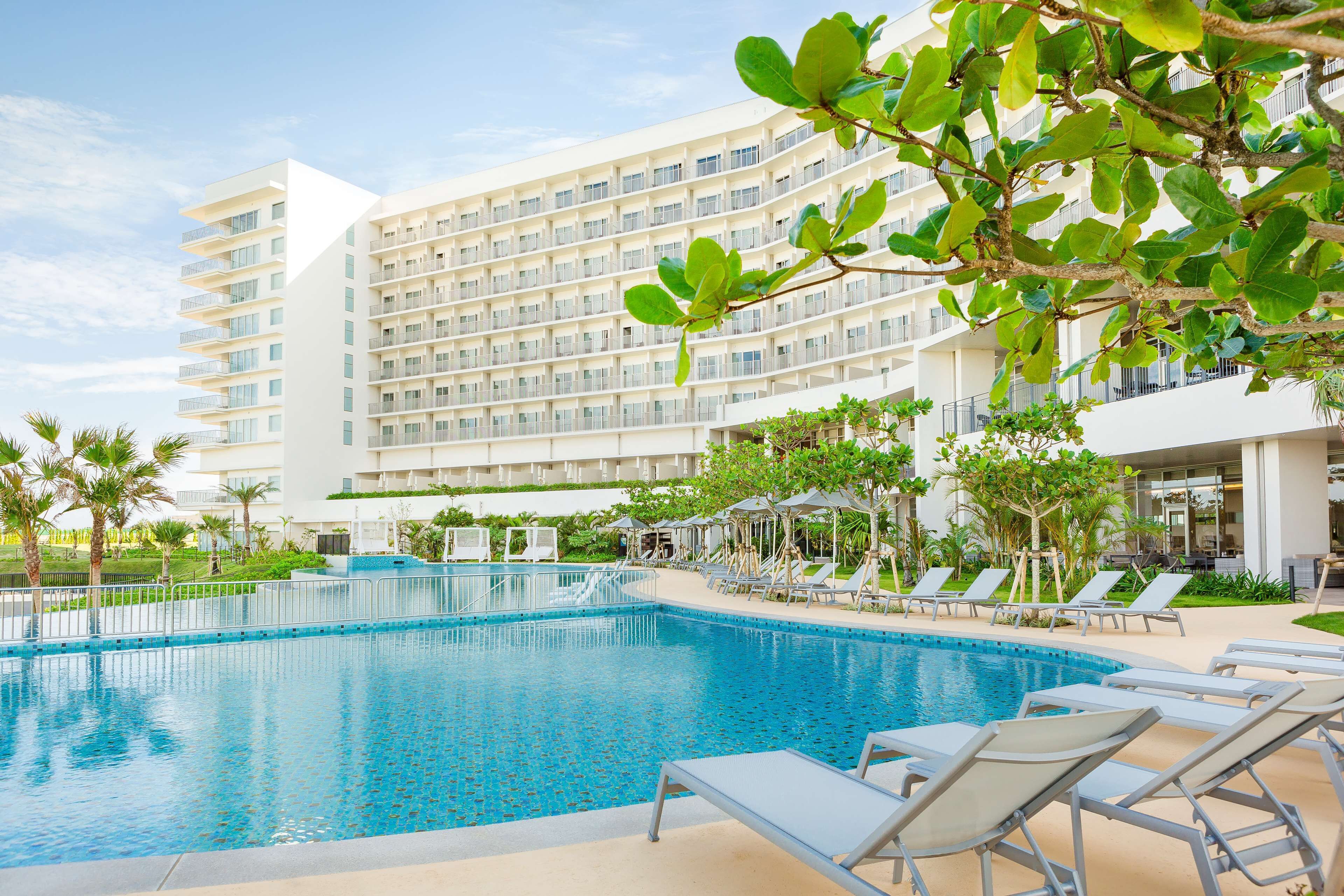 Un hotel con una piscina grande, varios balcones y sillones de descanso.