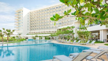 Un hotel con una piscina grande, varios balcones y sillones de descanso.