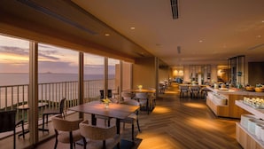 A modern dining area with a view of the ocean, wooden flooring, and a buffet setup. - Hilton Okinawa Sesoko Resort (Motobu)