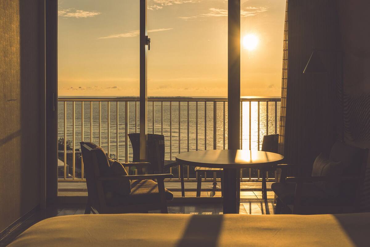 Habitación con balcón que da a una masa de agua al atardecer.