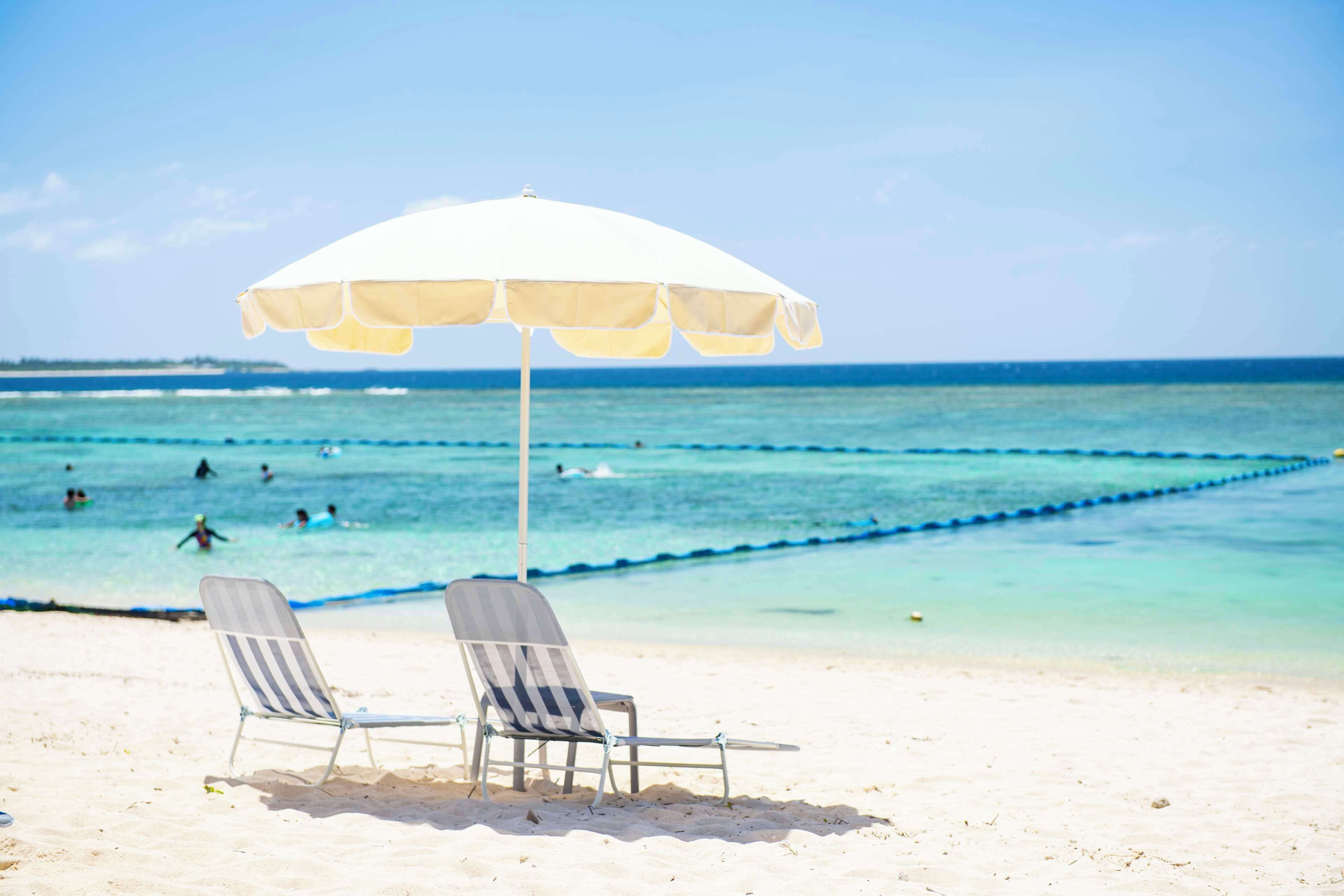 A beach with two striped lounge chairs and a white umbrella.