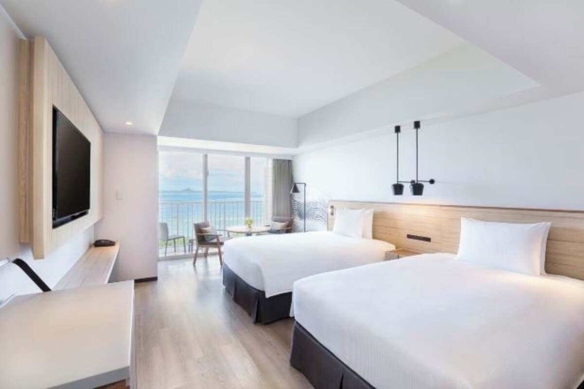 A modern hotel room with two beds, a TV, a balcony with a view, and a dining area.