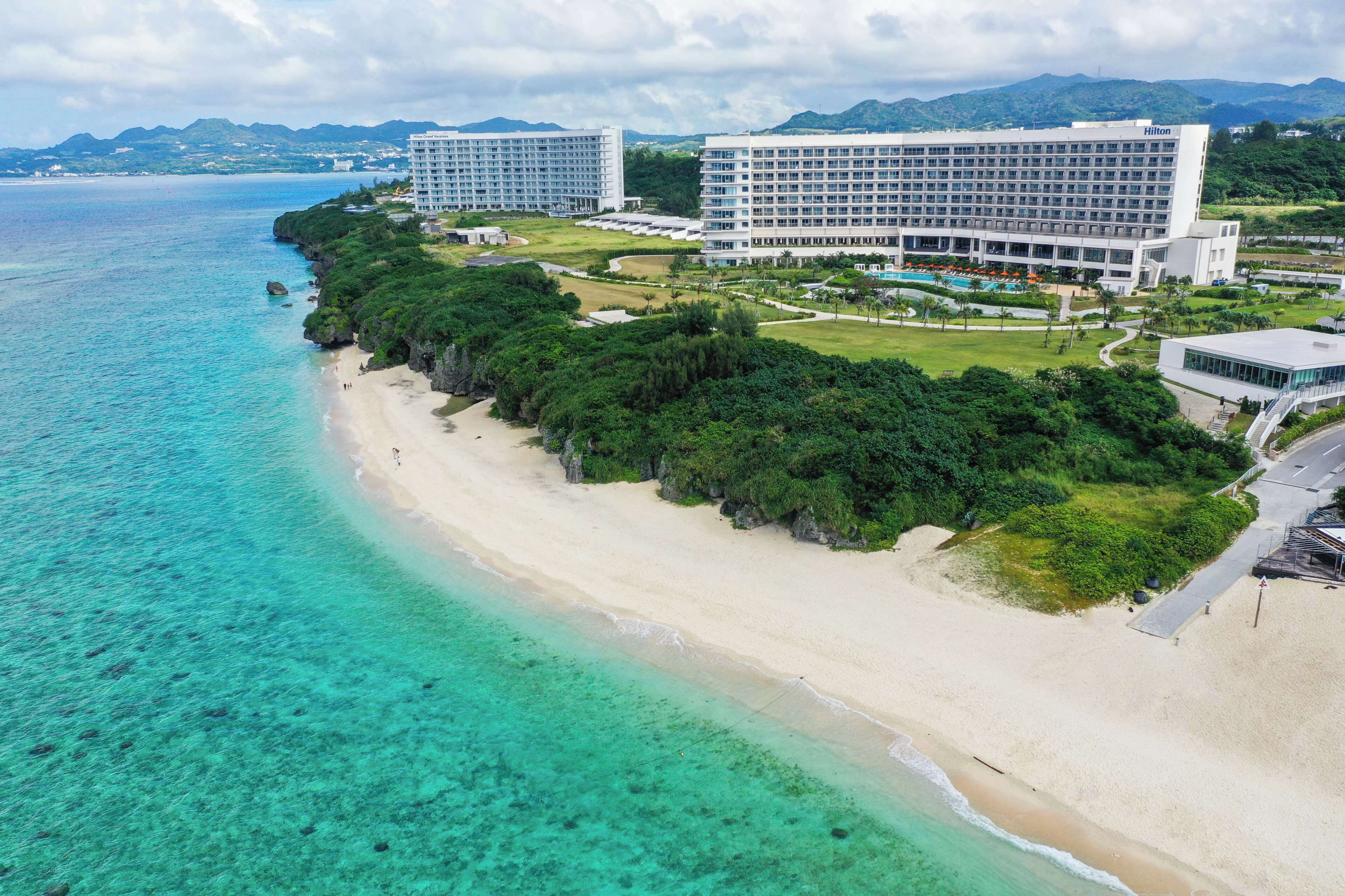 A beachfront hotel with multiple buildings, a clear view of the ocean, and a well-maintained lawn area.