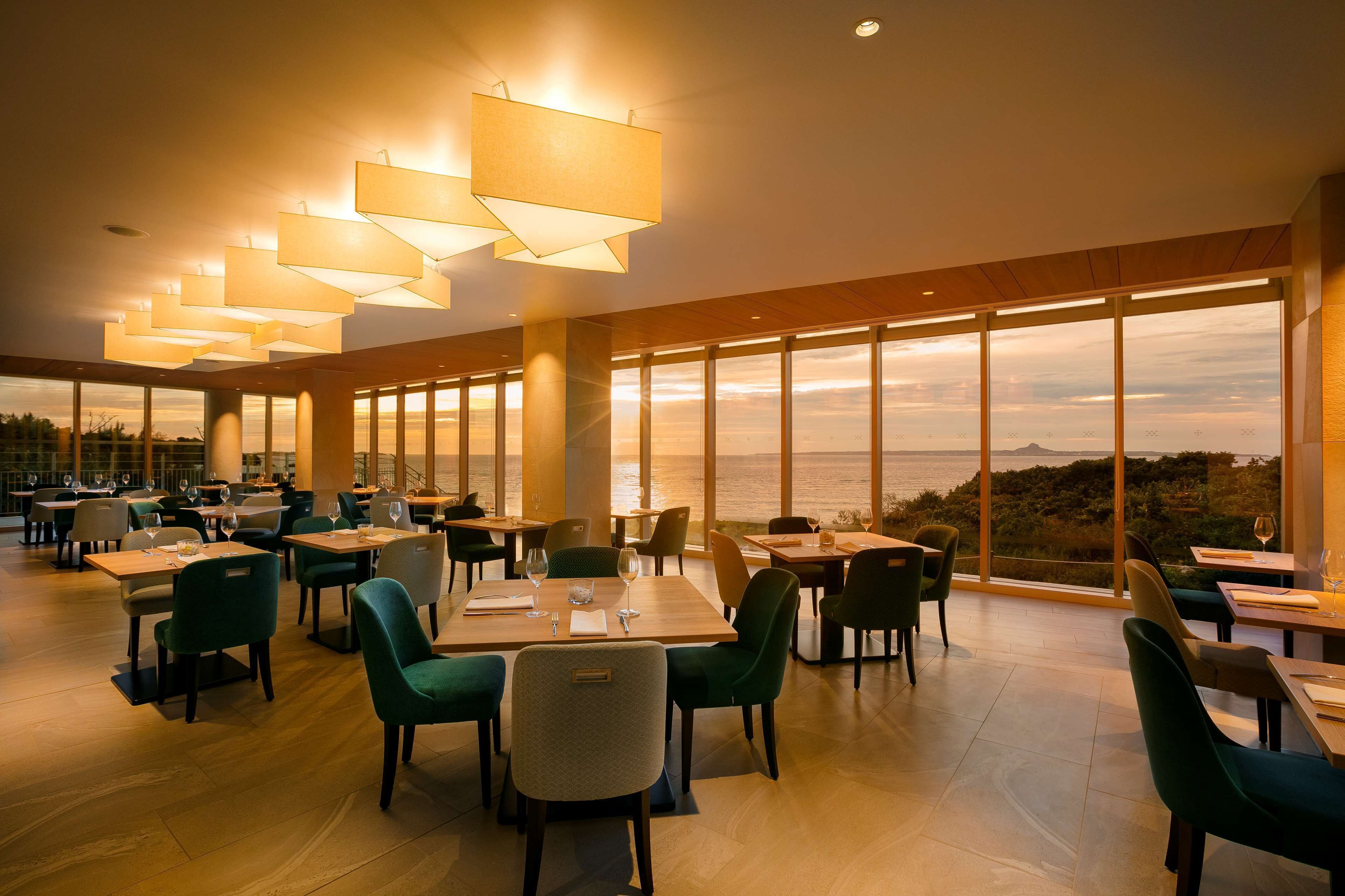 A spacious dining area with tables and chairs, large windows offering a view of the sea, and pendant lighting.