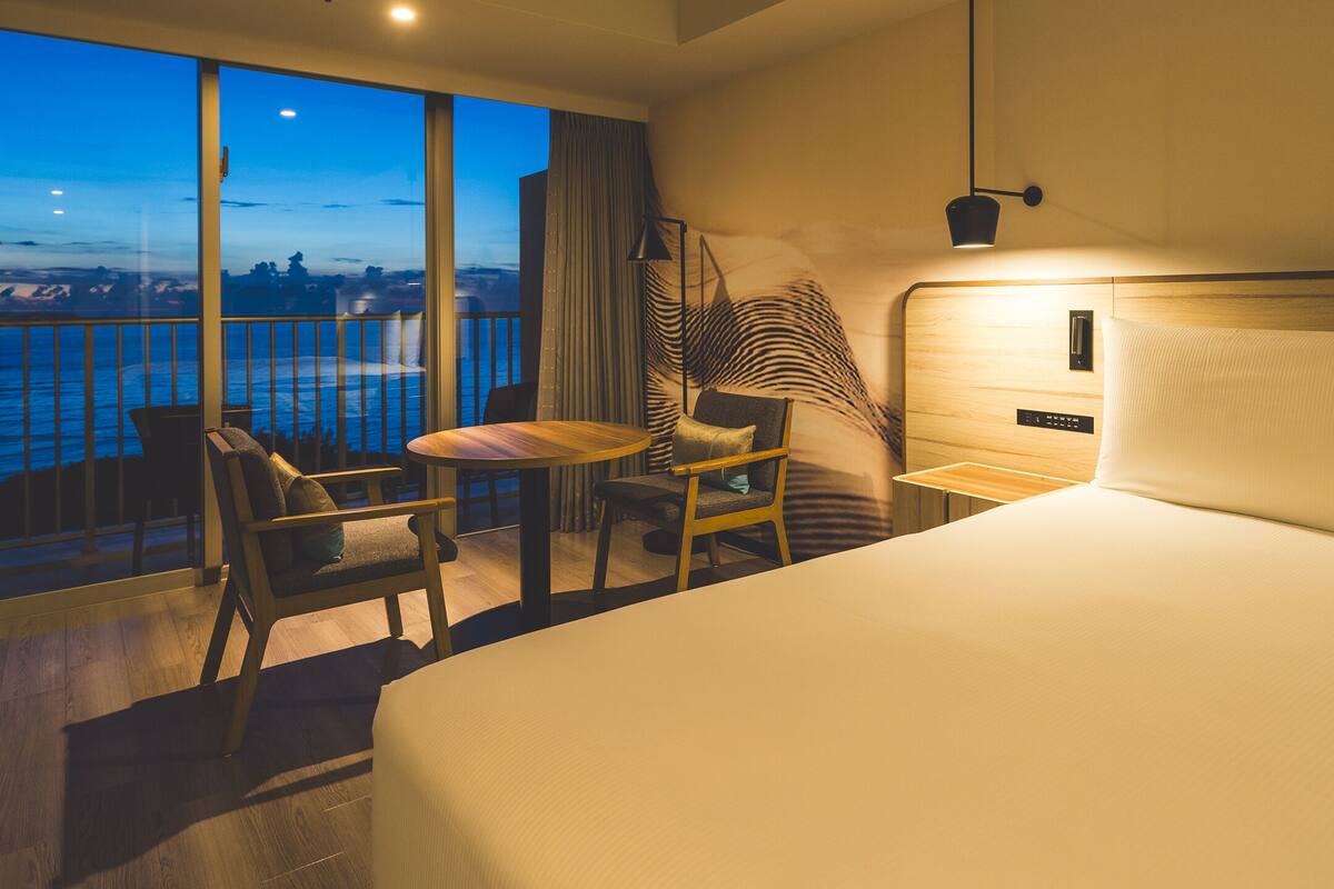 Habitación de hotel con una cama grande, un escritorio, una silla y vista al mar.